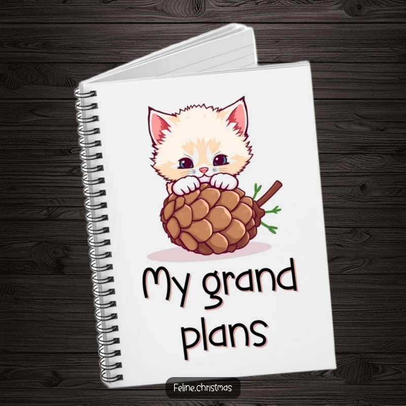 Funny fluffy kitten pouncing on a rolling pinecone, a notebook for jotting down playful thoughts.